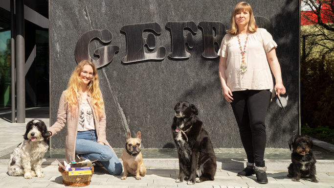 Gruppenbild mit Vorstand Sandra und Mitglied Marina vor dem GEFRO-Brunnen mit vier Hunden